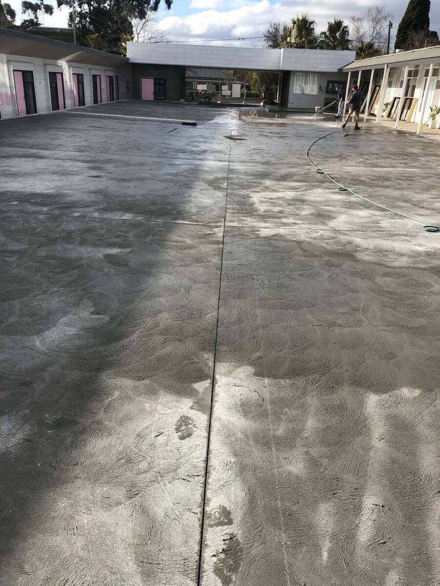 Crew washing down a large burnished concrete courtyard slab